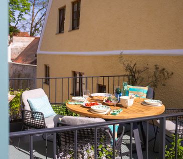 Sonniger Balkon mit rundem Gartentisch und vier gepolsterten Gartenstühlen.