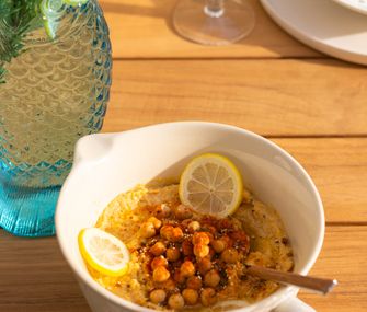 Hummus in einer weißen Schale auf Gartentisch im Freien.