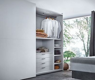 Weißer Schiebetürenschrank, bei dem eine Seite offen ist und Kleidung zeigt