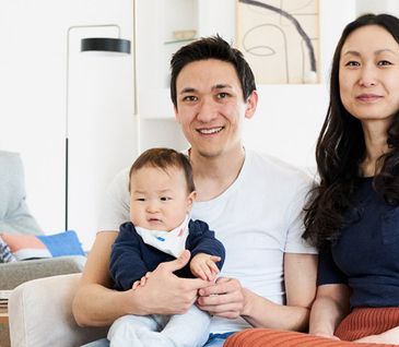 Vater und Mutter sitzen auf Sofa mit ihrem kleinen Baby auf dem Schoß