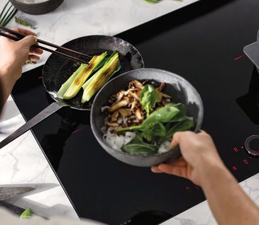 Eine Person brät Gemüse auf einem Kochfeld 