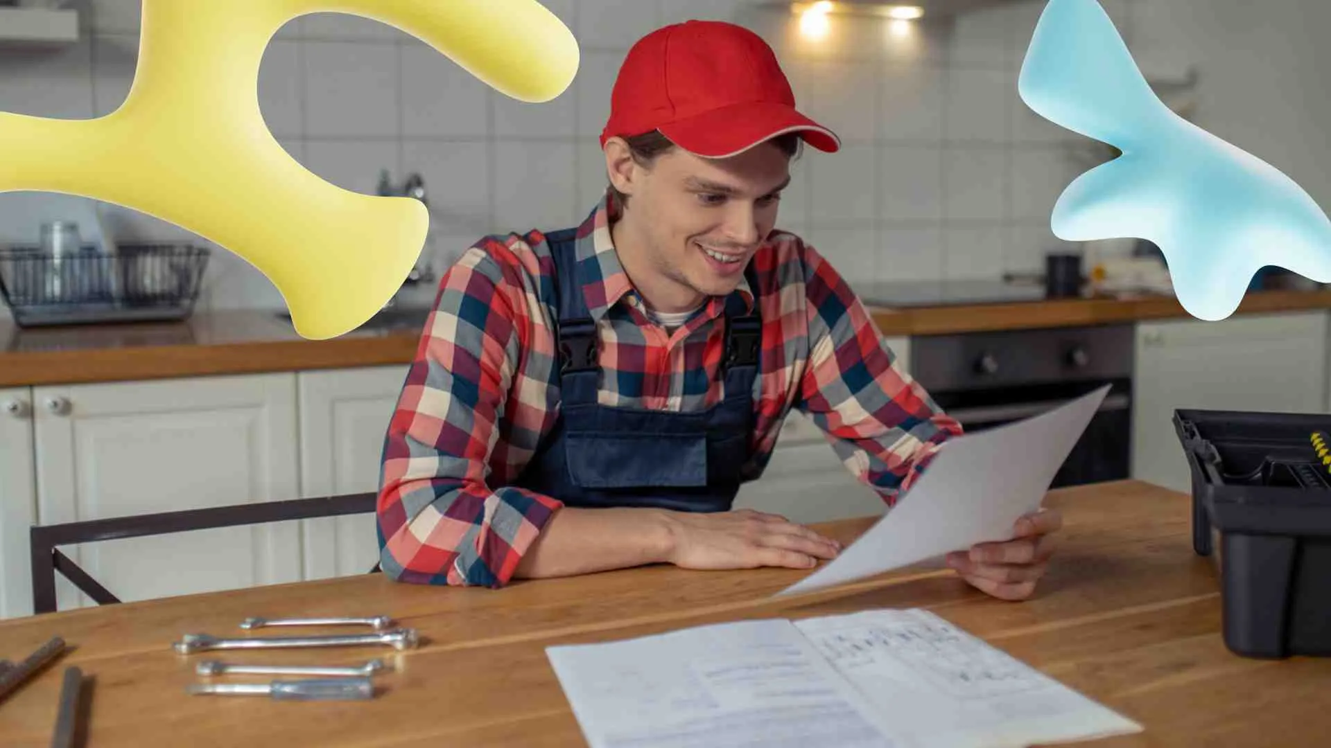 A smiling male worker in a red cap and overalls reviews papers at a kitchen table with tools. Abstract yellow and blue shapes float.