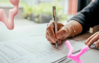 A hand signs a document with a silver pen on a desk, flanked by two floating pink abstract wavy shapes.