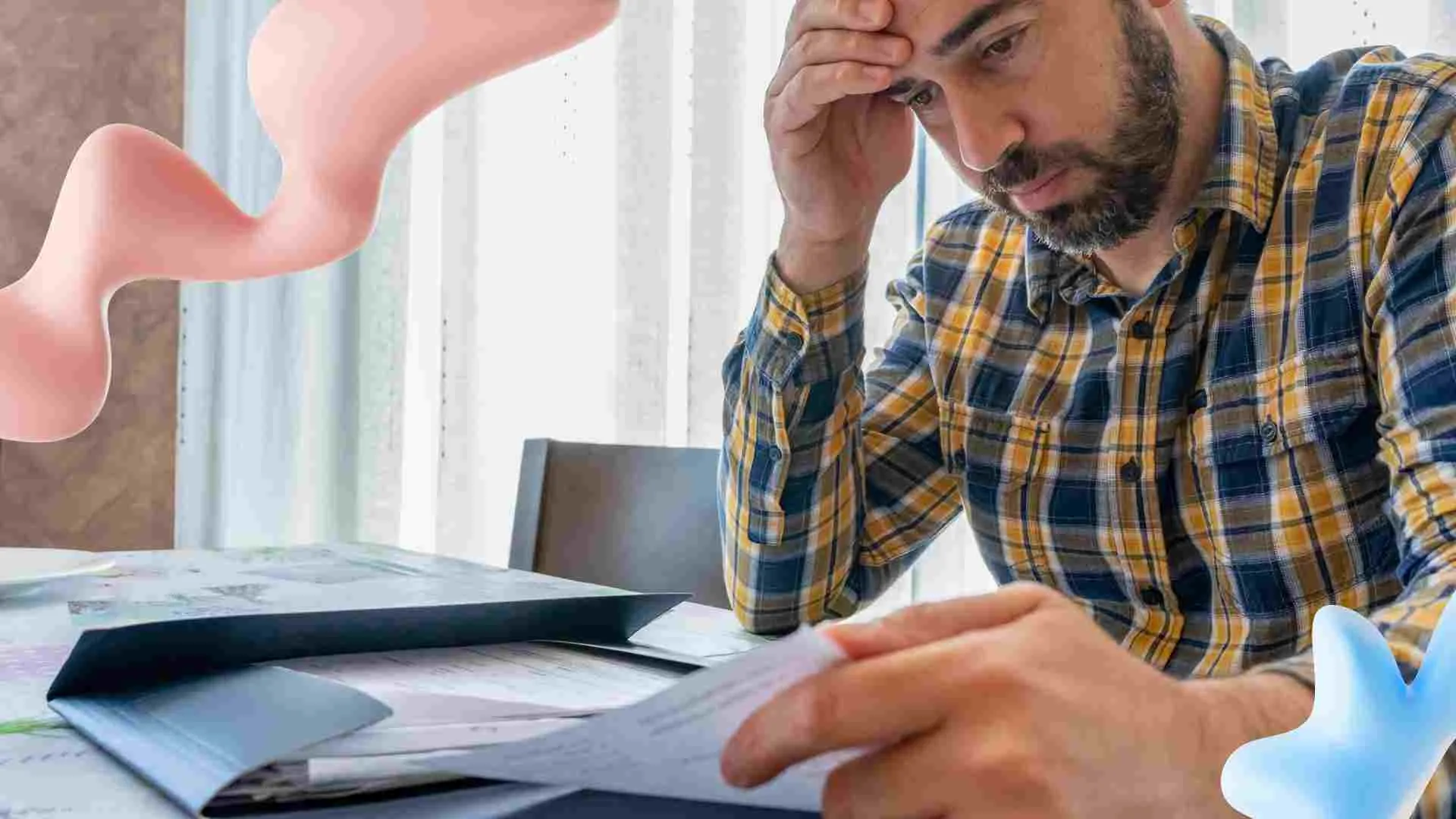 Stressed bearded man in a plaid shirt reading documents at a table, with abstract pink and blue shapes.