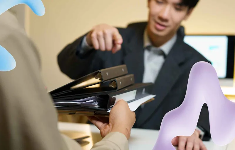 A person hands a stack of binders to a smiling businessman in a suit at a desk, overlaid with abstract blue and purple shapes.