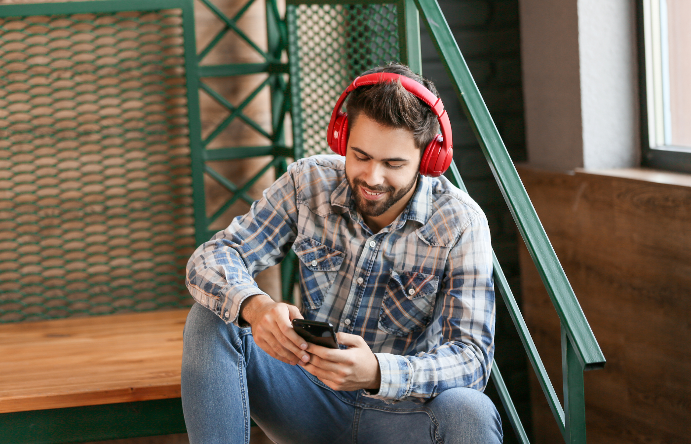 The image shows a man listening to an audiobook with red headphones. He looks happy.