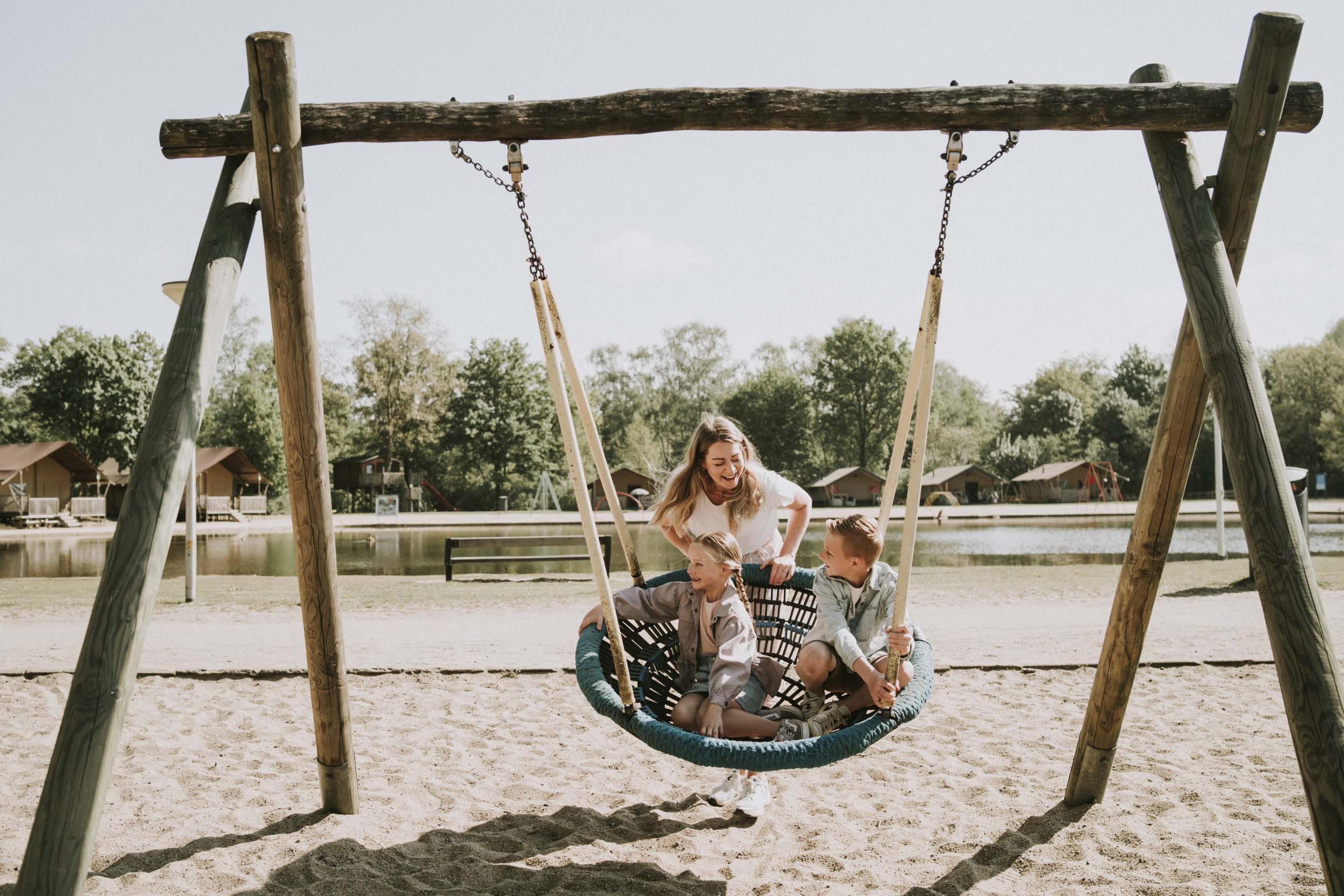 Moeder en kinderen spelen met een schommel in de speeltuin van Vakantiepark Dierenbos