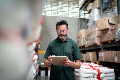 Man with glasses standing in warehouse, looking at iPad