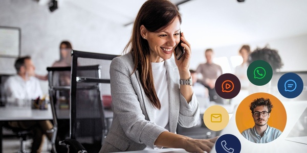 Kundenservice-Mitarbeiterin im Büro am Telefon, lächelt in ihren Laptop. Überlagerung aus Kommunikationssymbolen und dem Profilfoto eines Kunden. Moderne Kundenkommunikationslösungen erlauben den Kontakt über verschiedene Kanäle und bieten neben E-Mail und Telefon auch WhatsApp, RCS oder SMS an.