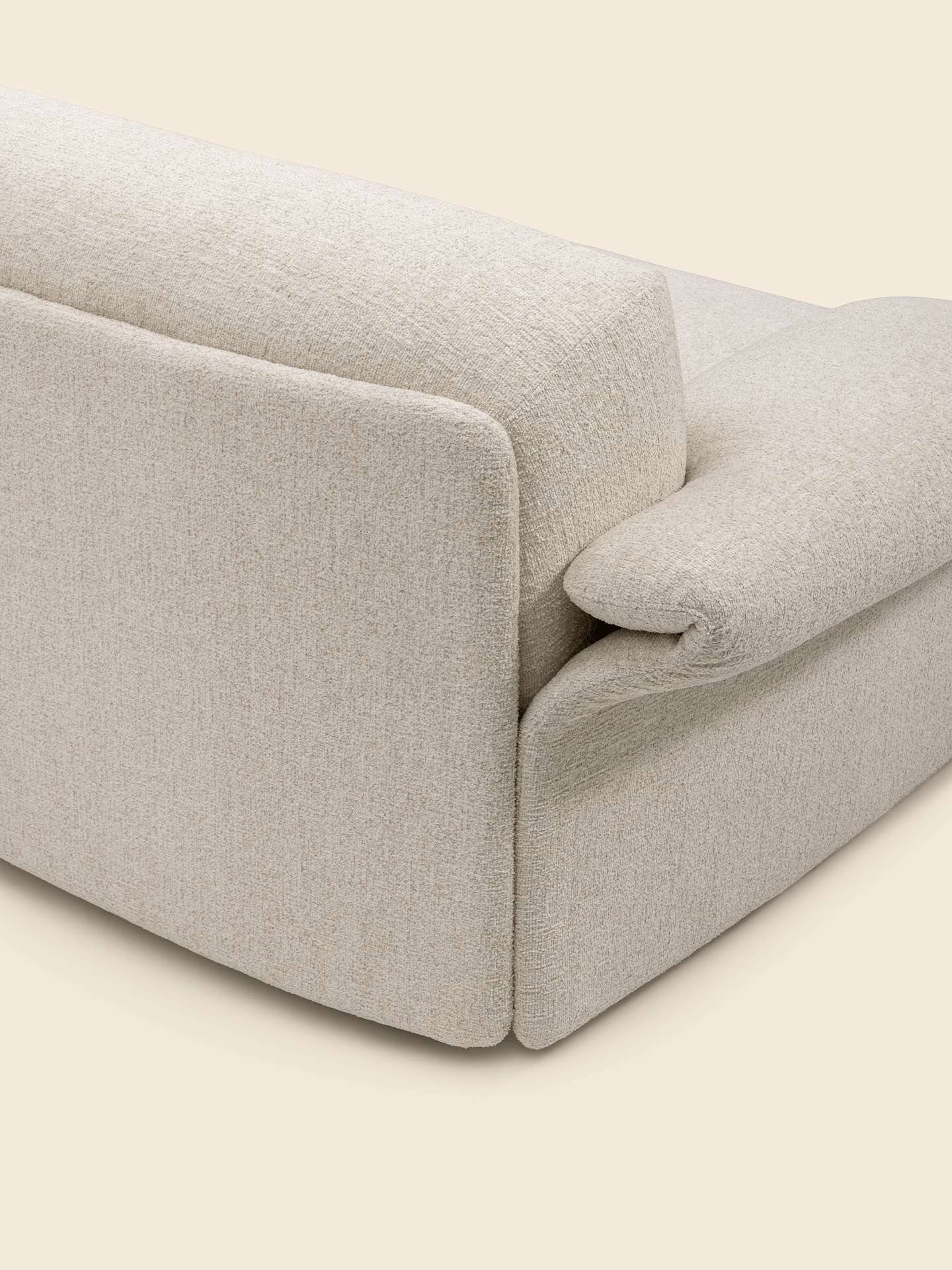 Close-up of a beige fabric sofa corner, showcasing its textured upholstery and padded armrest against a light background.