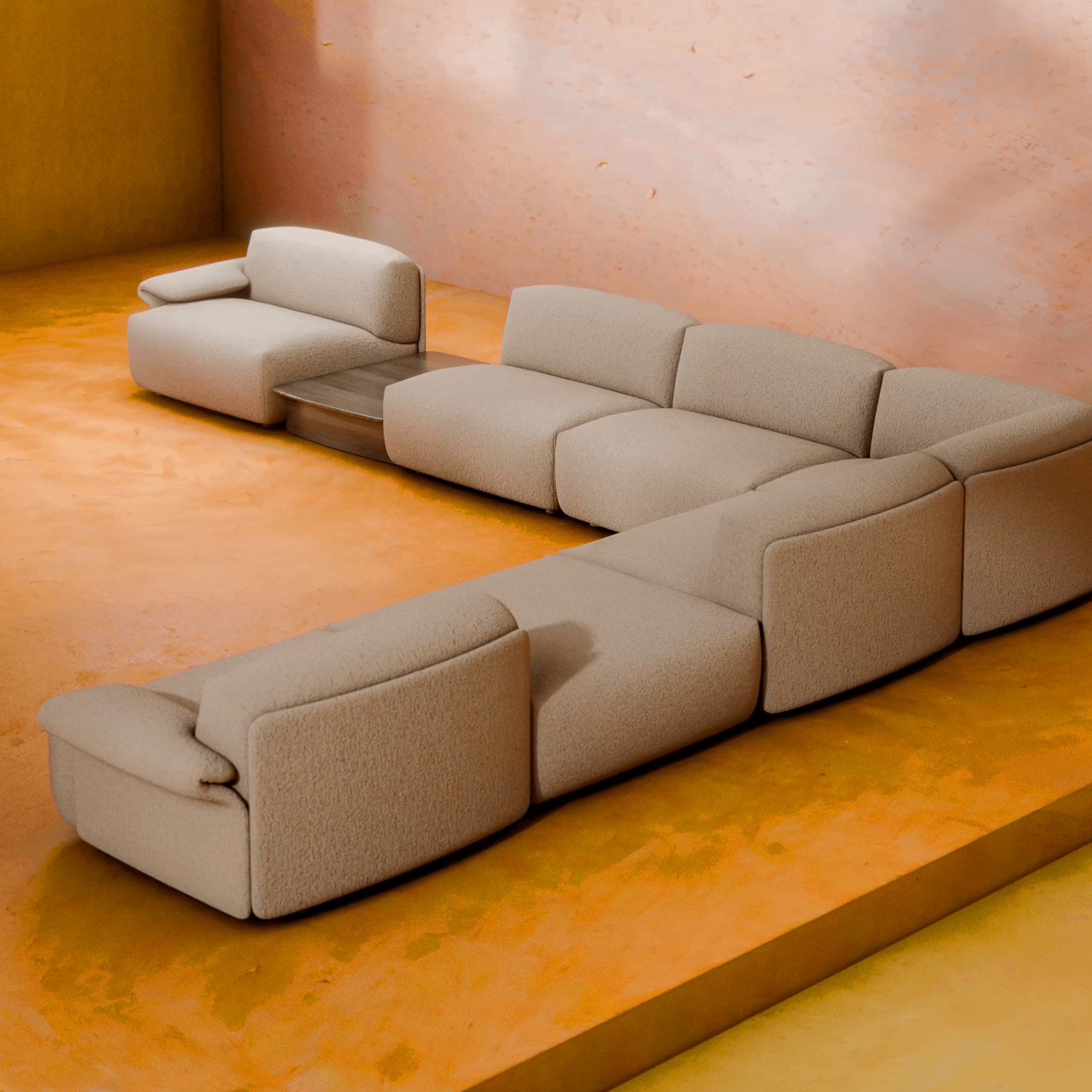 Modern L-shaped beige sectional sofa on a warm-toned floor, against a peach wall, featuring a built-in wooden side table.