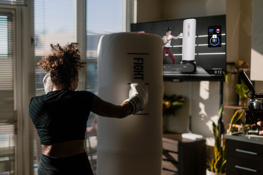 A woman punches the FightCamp bag at home while a class plays on her TV