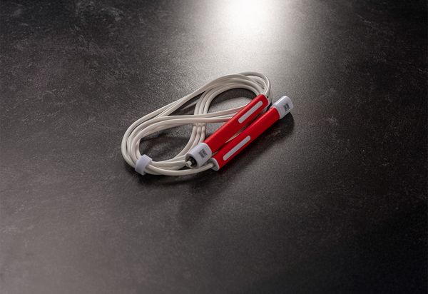 Red and white jump rope with plastic handles coiled neatly on a dark, textured surface.