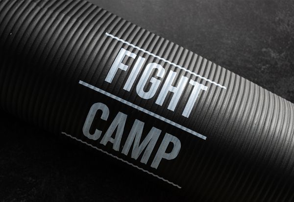 Close-up of a textured black exercise mat with the words "FIGHT CAMP" in bold white letters against a dark background.