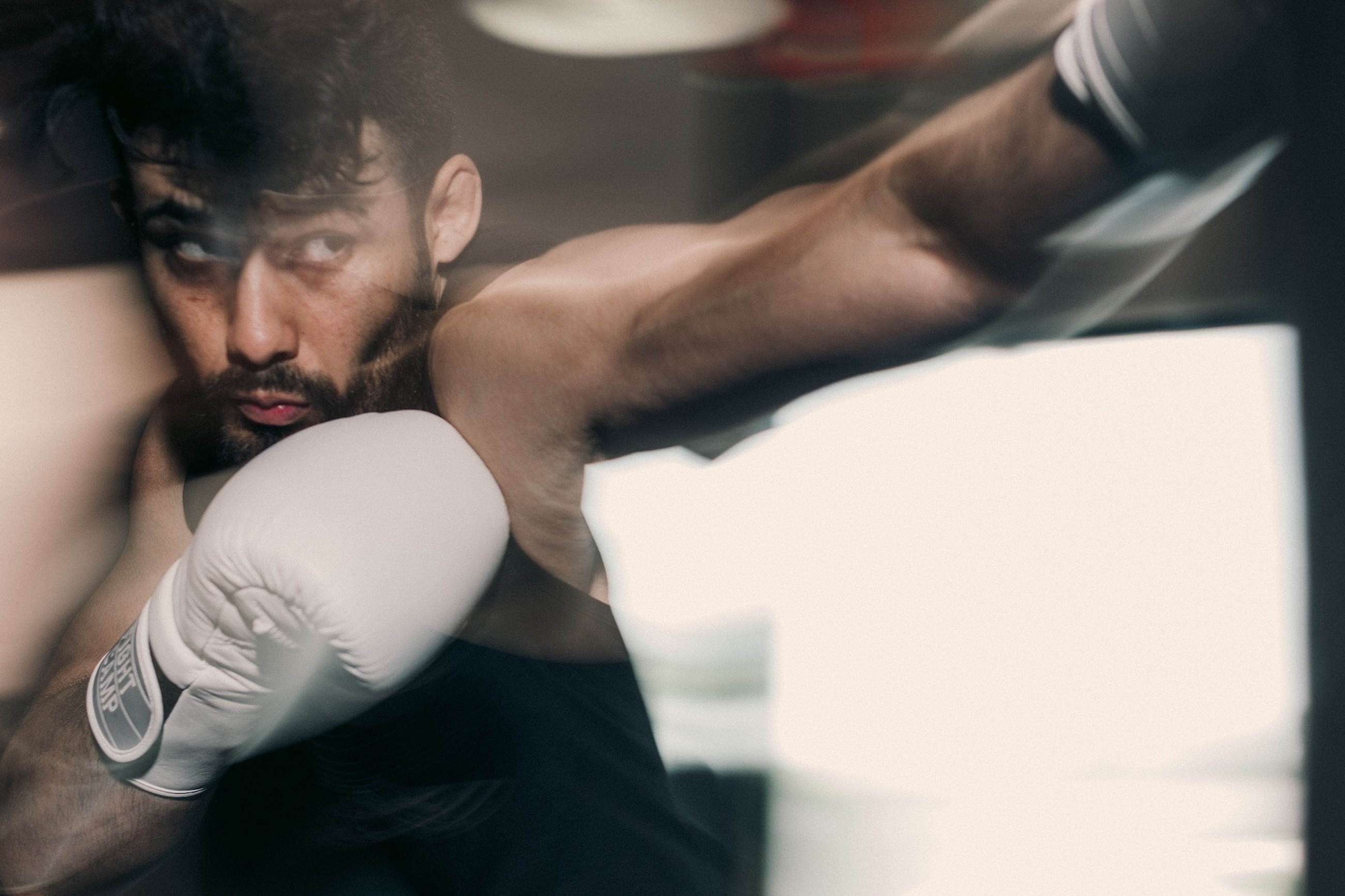 Boxer in motion, wearing white FightCamp gloves, focused intensely while throwing a punch. Blurred background enhances the dynamic movement.