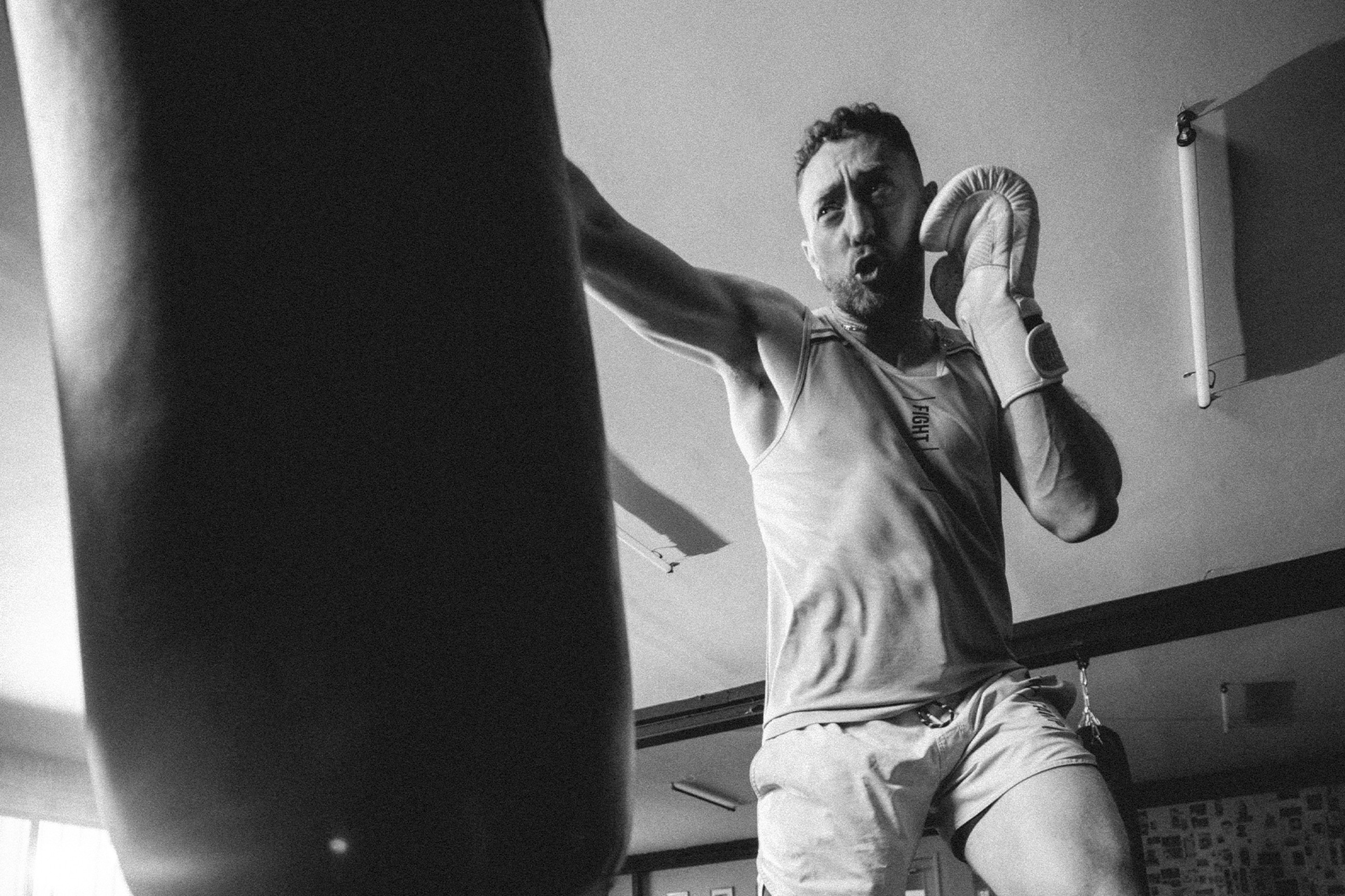Man in boxing gear intensely trains with a punching bag in a gym. Black and white image.