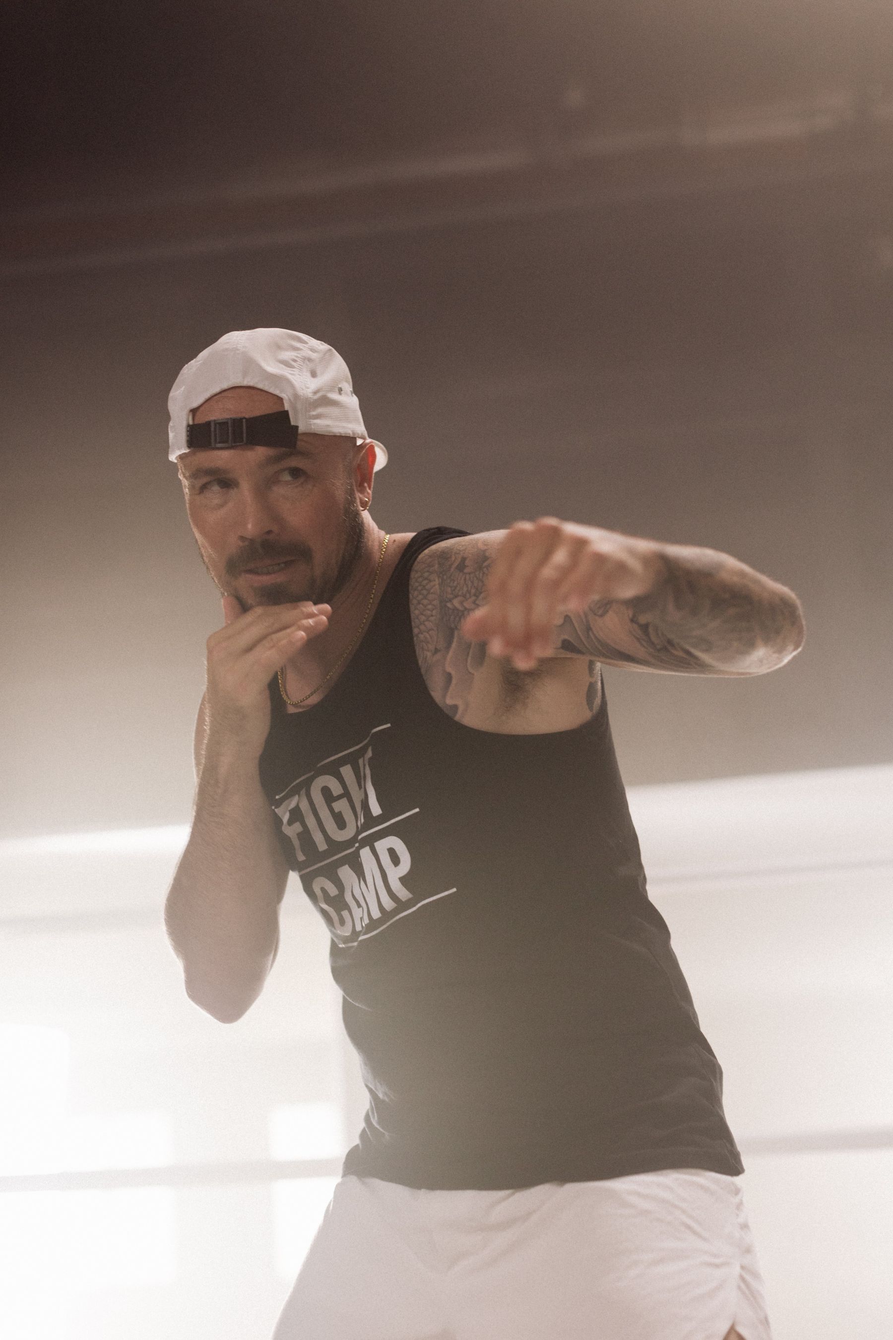 Man in a tank top and cap practicing a boxing stance in a well-lit gym, with focus and determination.