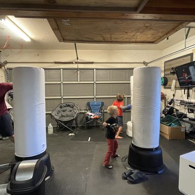 Children and father wearing boxing gloves while hitting FightCamp bag in garage