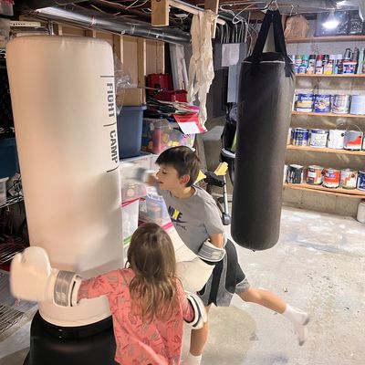 children wearing boxing gloves while hitting FightCamp bag in basement