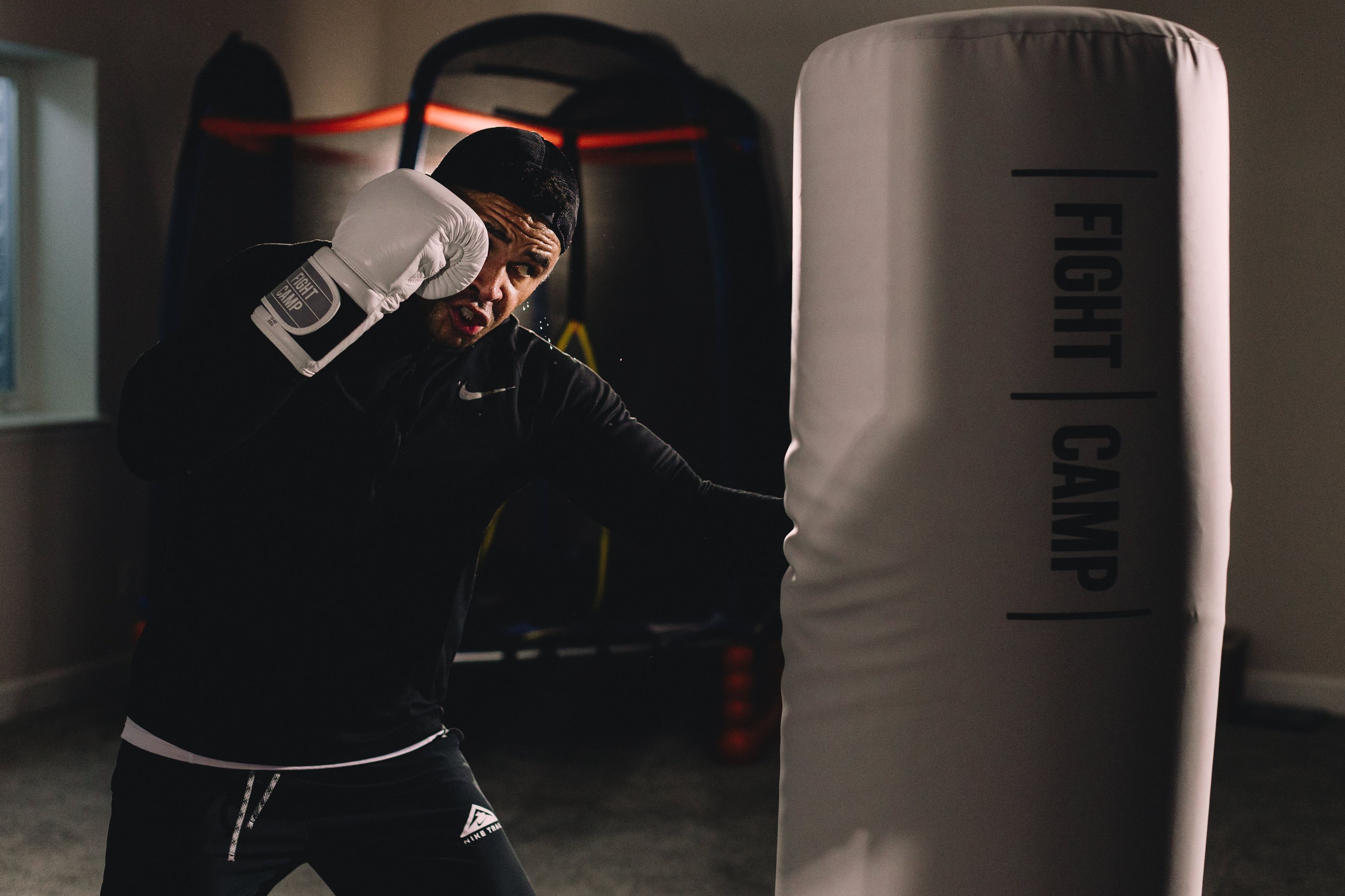 Person wearing boxing gloves practicing punches on a white punching bag labeled "Fight Camp" in a dimly lit room.