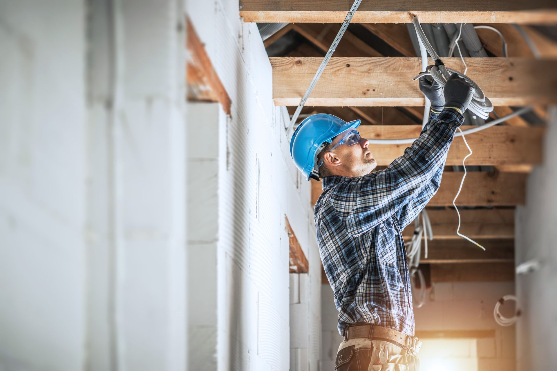Image of an electrician install something in the ceiling on a construction site wearing a blue hardhat