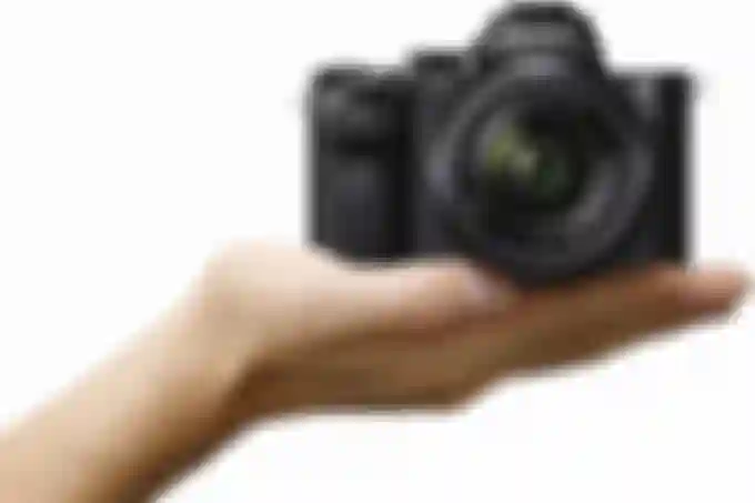 The Sony Alpha a7 IIK in a person's hand against a white background.