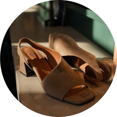 Tan suede heeled sandals with open toes and slingback design displayed on a sunlit surface.