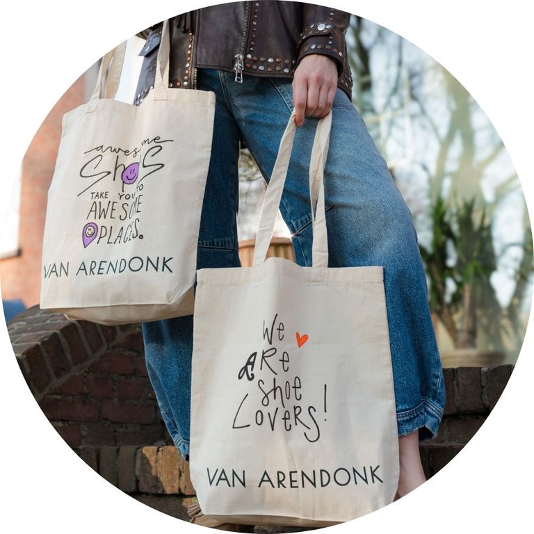 Two tote bags with playful text and heart designs are carried by a person in casual denim jeans and a leather jacket.