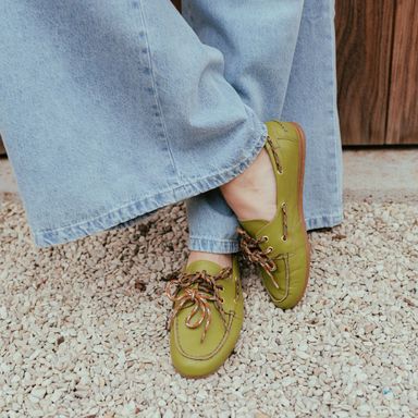 Person wearing green loafers with patterned laces, paired with light blue wide-leg jeans, standing on gravel.
