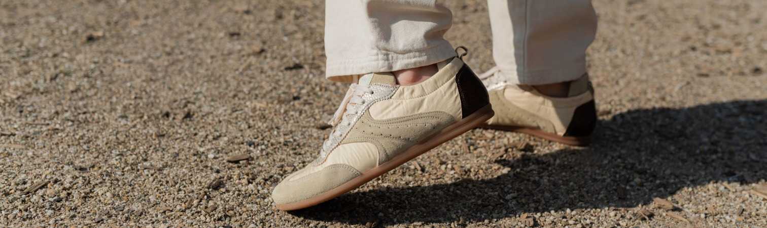 Persoon met lichtgekleurde broek en laag uitgesneden ballerina sneakers met elastische hiel op grindpad