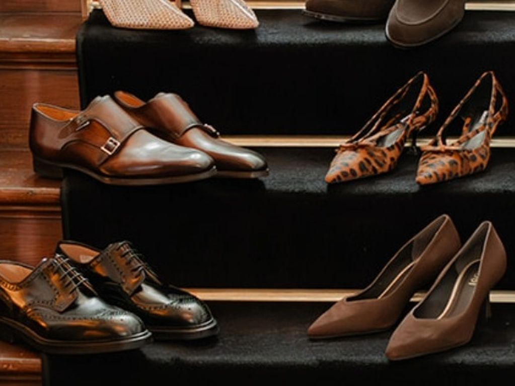 ChatGPT zei:  Verschillende paren schoenen, waaronder nette modellen en hoge hakken, staan netjes opgesteld op een houten trap met een donkere loper.