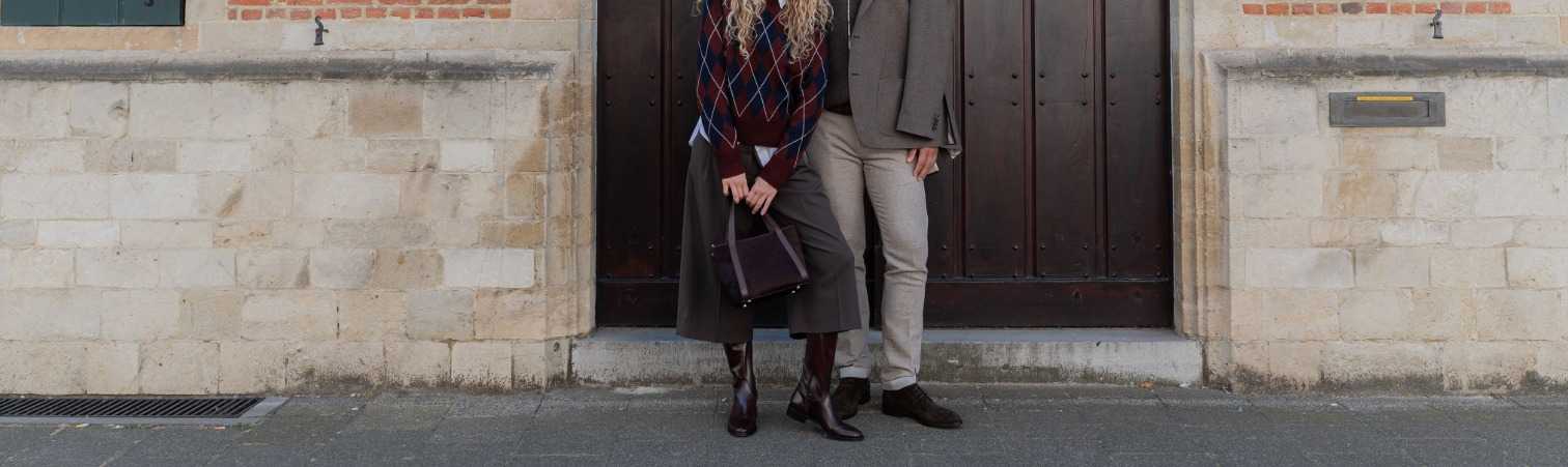 Man en vrouw in bruin, beige, taupe en grijze kleding op stoep voor grote houten deur