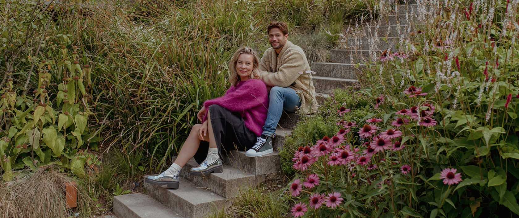 Man en vrouw met schoenen uit de nieuwe schoenencollectie herfst winter 2023 2024 zittend op trap tussen groen gras en bloemen