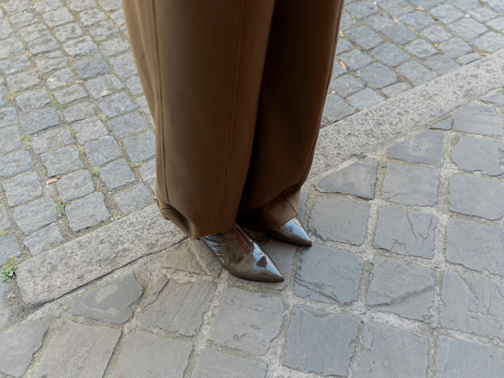 Bovenaanzicht groene lakleren enkellaarsjes met puntige neus en wijde khakikleurige pantalon op kasseien