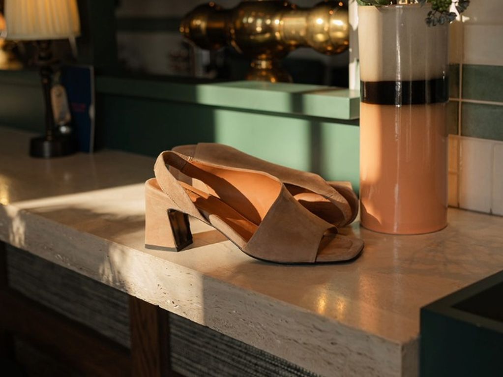 Beige suède sandalen met hak op marmeren blad naast een vaas