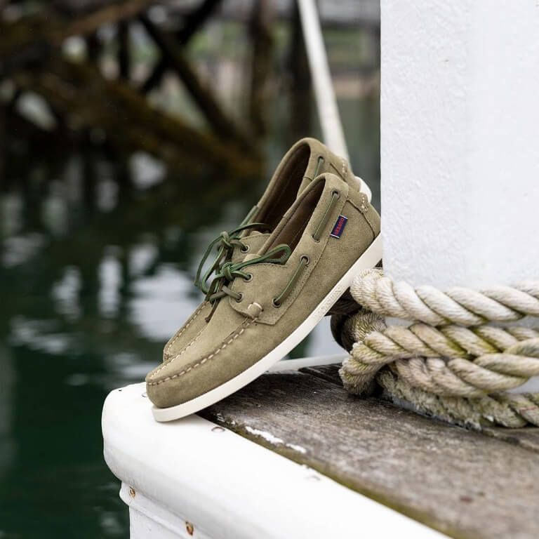 Khaki groene bootschoenen op houten ondergrond tegen witte paal met scheepstouw eromheen