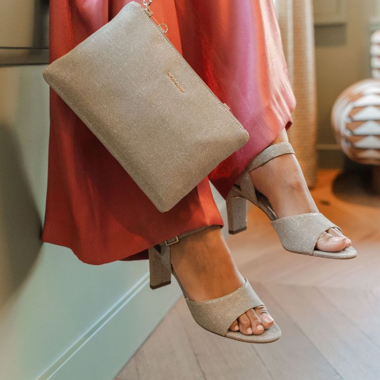 Vrouw met lange jurk en tassen en blokhakken zittend op een bankje