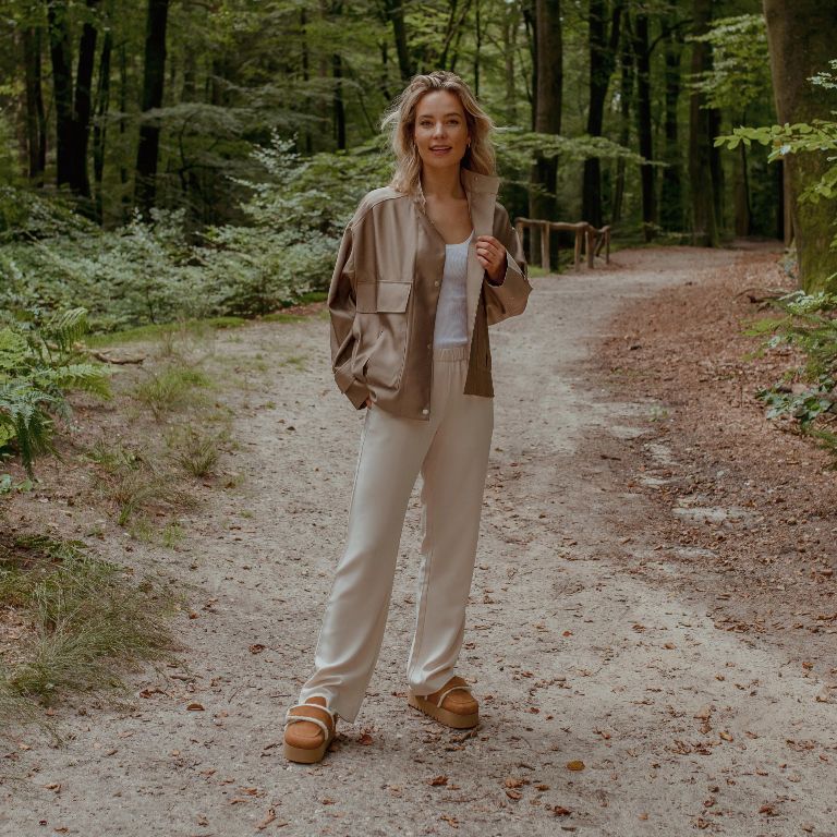 Vrouw in bos met bontgevoerde clogs gecombineerd met lichtgekleurde wijdvallende broek en beige jack