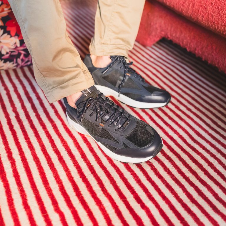 man-draagt-herensneakers-nieuw-merk-bij-van-arendonk-met-zwarte-pantalon-op-kleurrijk-tapijt