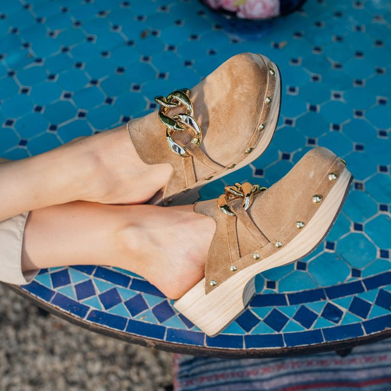 Rijkelijk versierde bruine clogs met gouden ketting en studs op blauwe mozaïek ondergrond