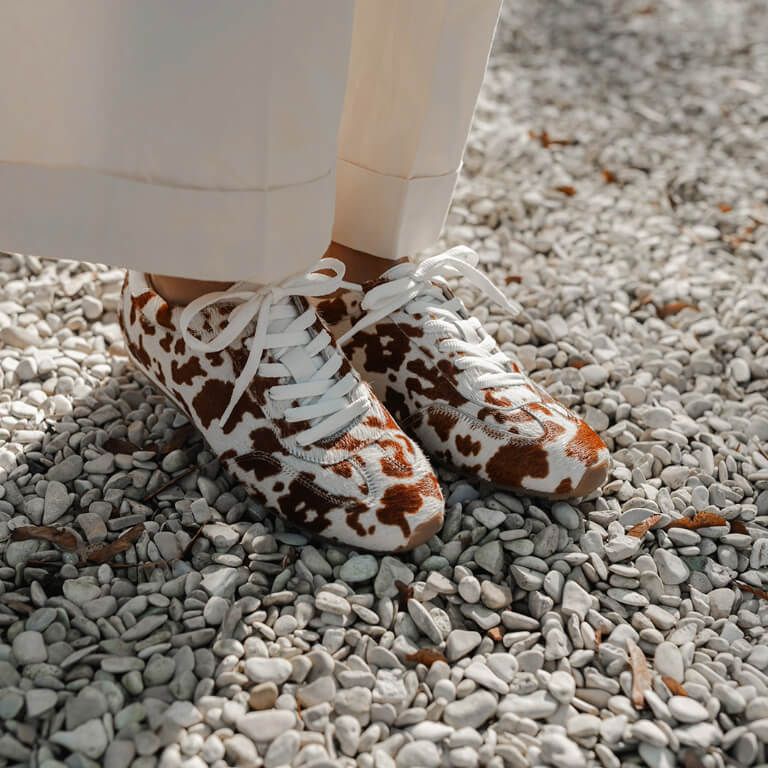 DWRS Label sneakers met koeienprint onder crèmekleurige omgeslagen broek op kiezelsteentjes