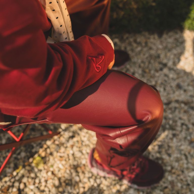 Close-up-van-donkerrode-outfit-met-leren-broek-gebreide-trui-en-sneakers-op-grindpad-in-de-zon