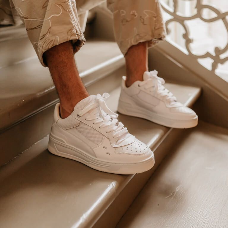 Close-up witte herensneakers onder beige broek met blote enkels