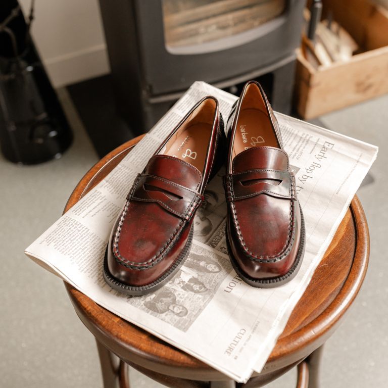 Leren loafers op een houten vintage tafel met een krant