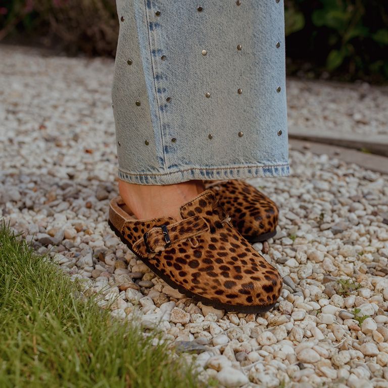 Clogs met panterprint onder lichtblauwe jeans met studs op kiezelsteentjes