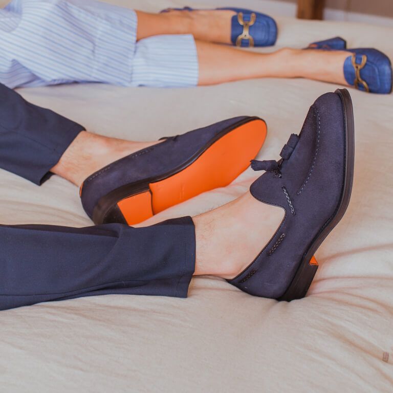 Donkerblauwe herenloafers met oranje zool onder donkerblauwe pantalon