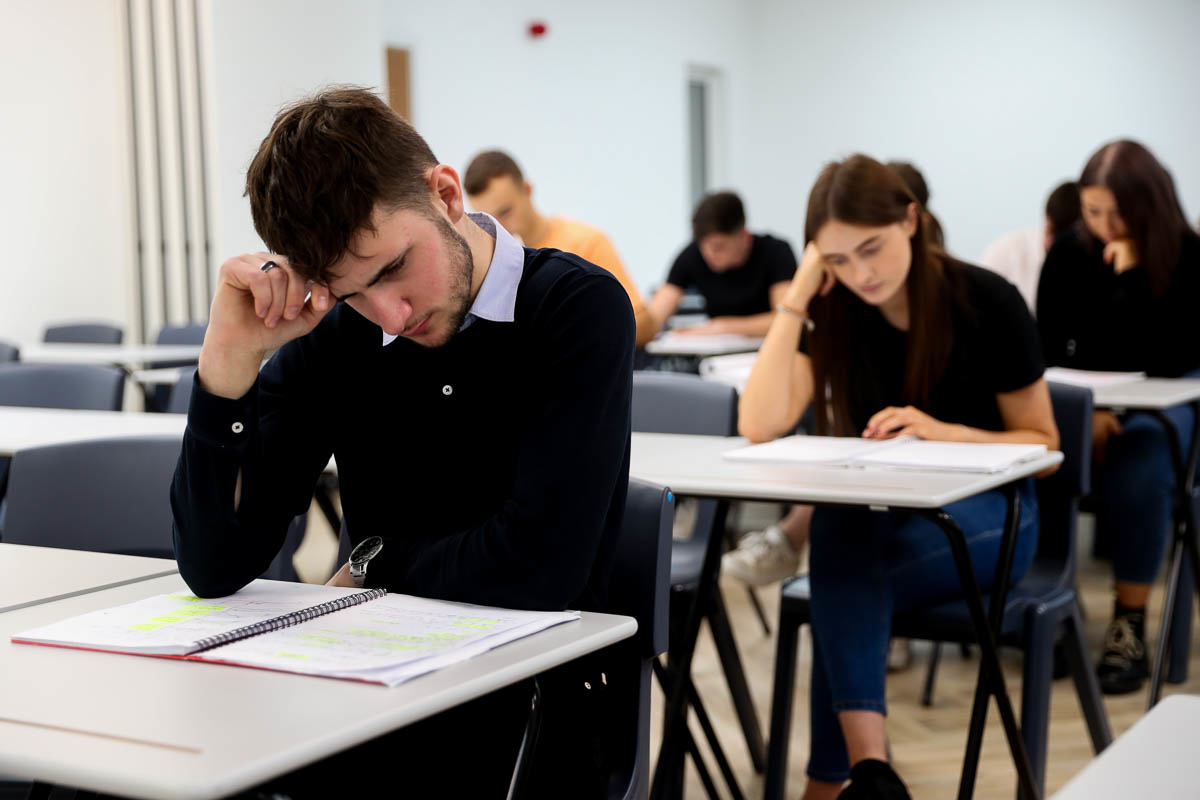 Students sitting at desks in a classroom, focused on writing in notebooks during a test or exam.