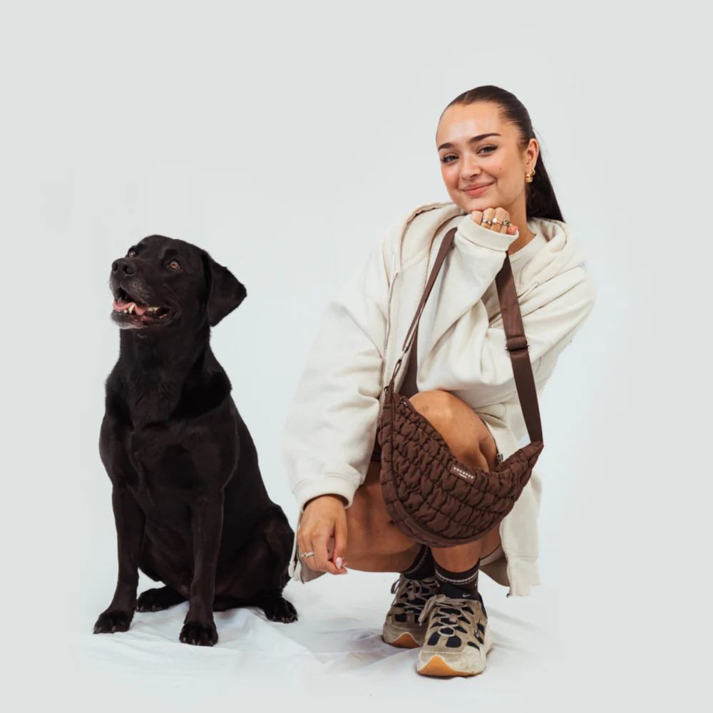 A woman posesd with her dog while showing off her brown Coco dog bag