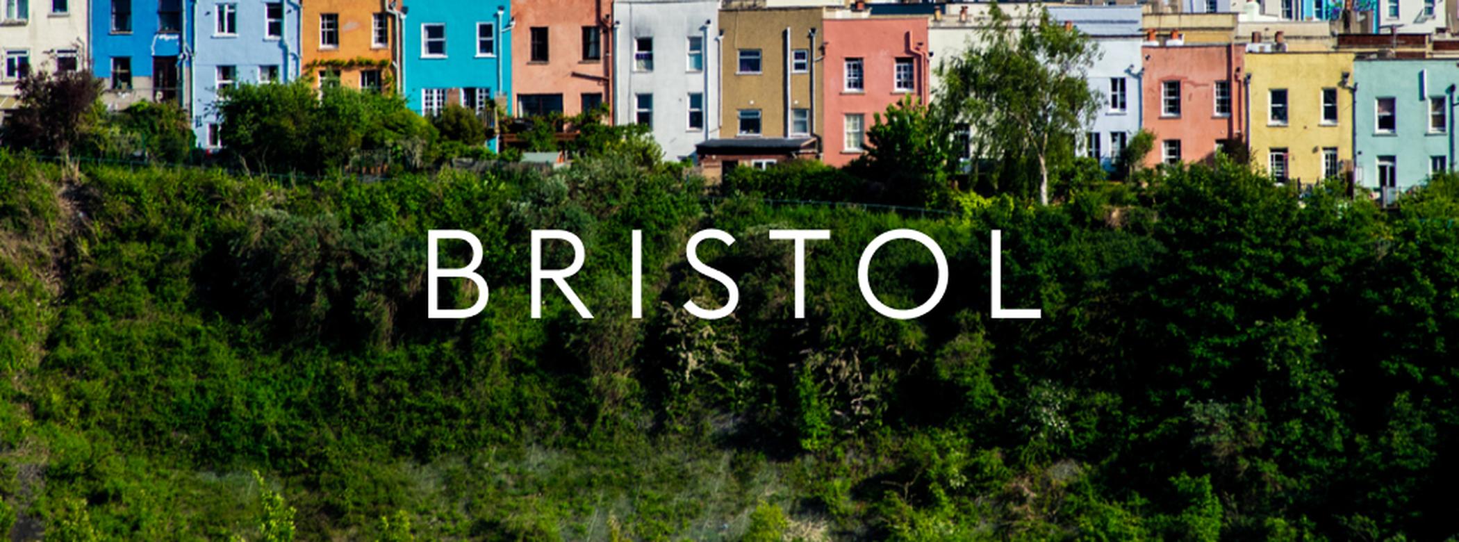 Colorful row of houses on a hill with lush greenery in front, and the word "Bristol" centered in the foreground.