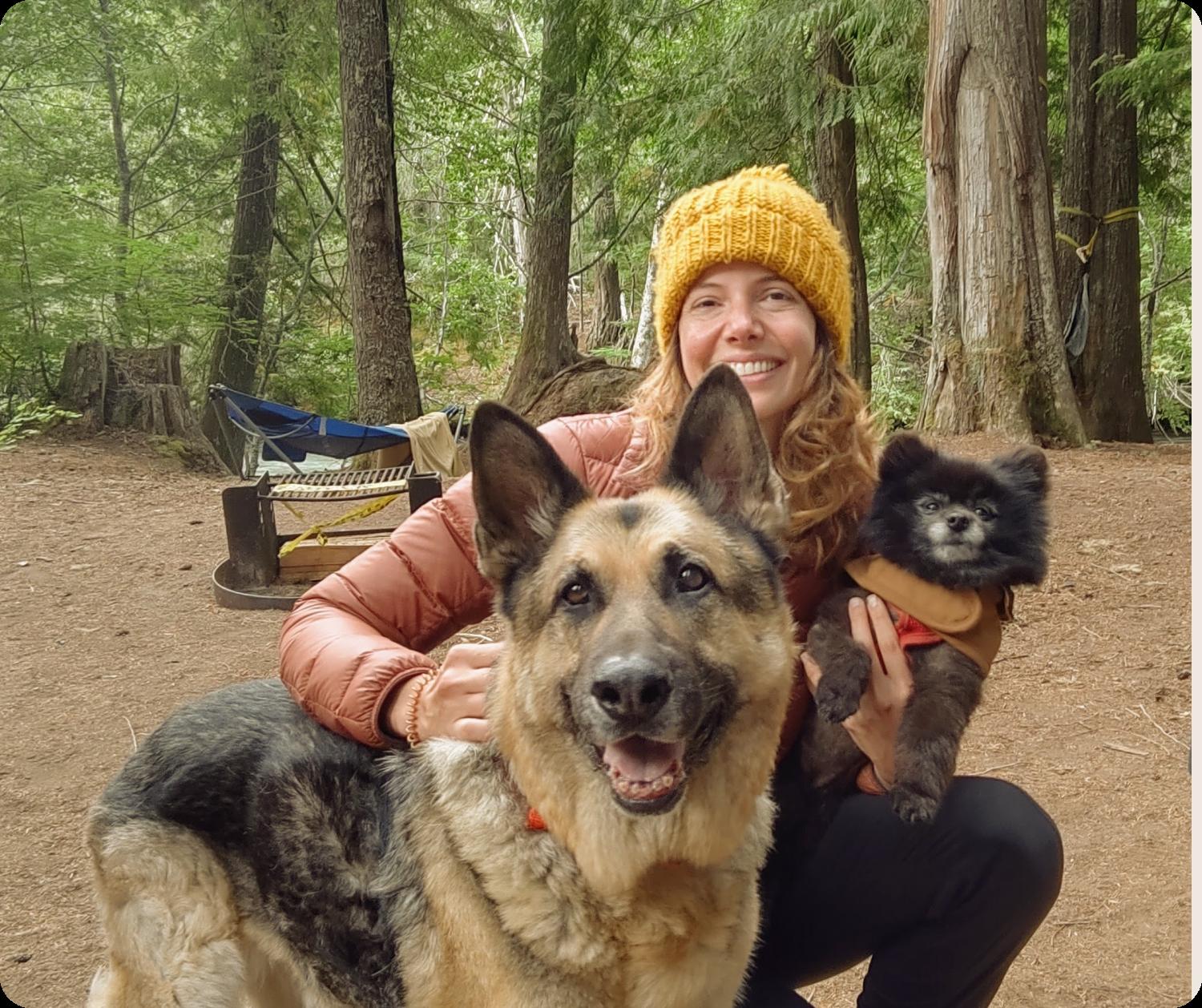 Woman kneels in woods with loyal German Shepherd and cute Pomeranian.